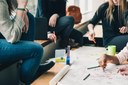Gruppenarbeit von drei Schülerinnen und Schülern, die an einem Tisch über Aufschriebe gestikulieren und diskutieren.